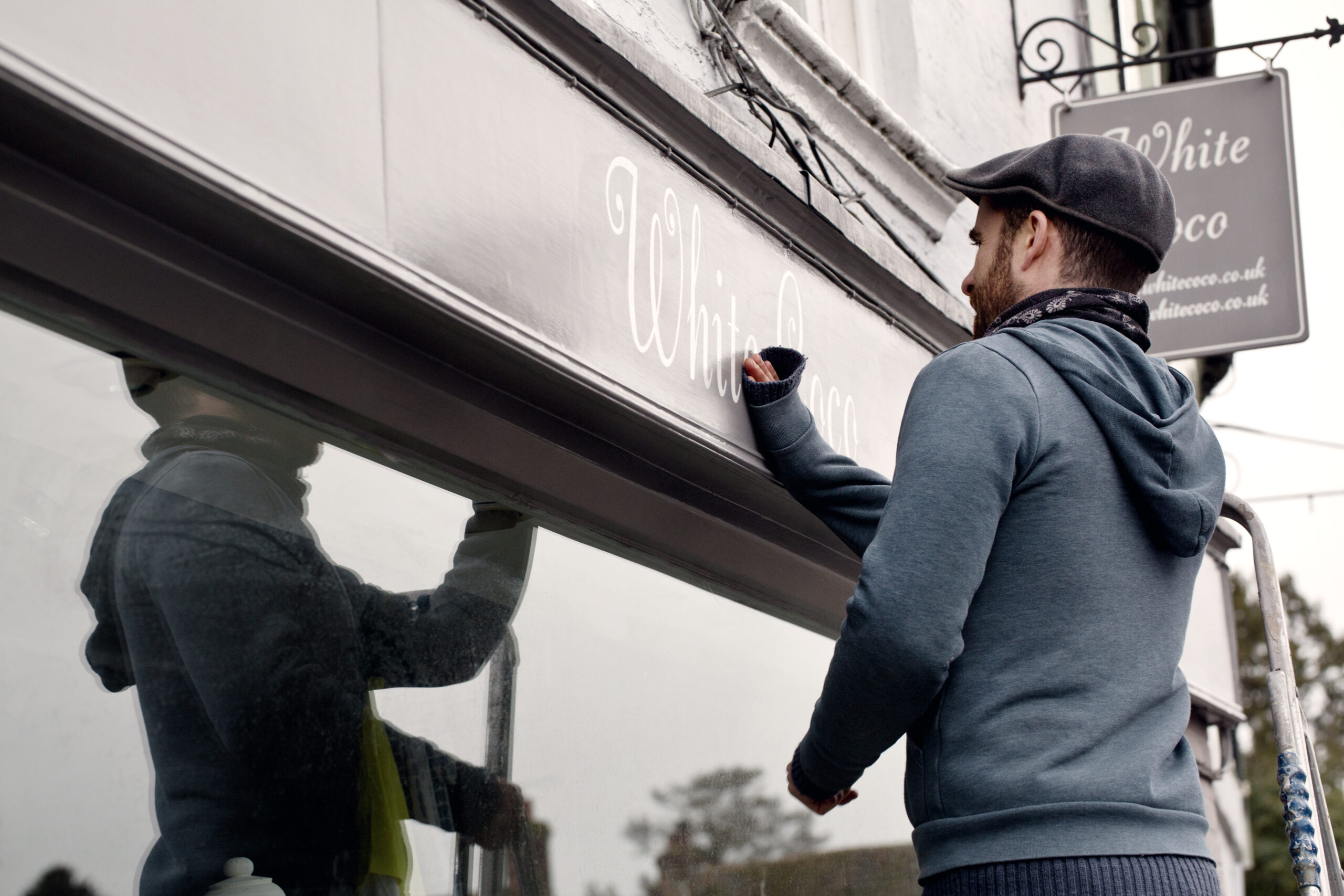 Man applying or removing vinyl lettering on a storefront window sign.