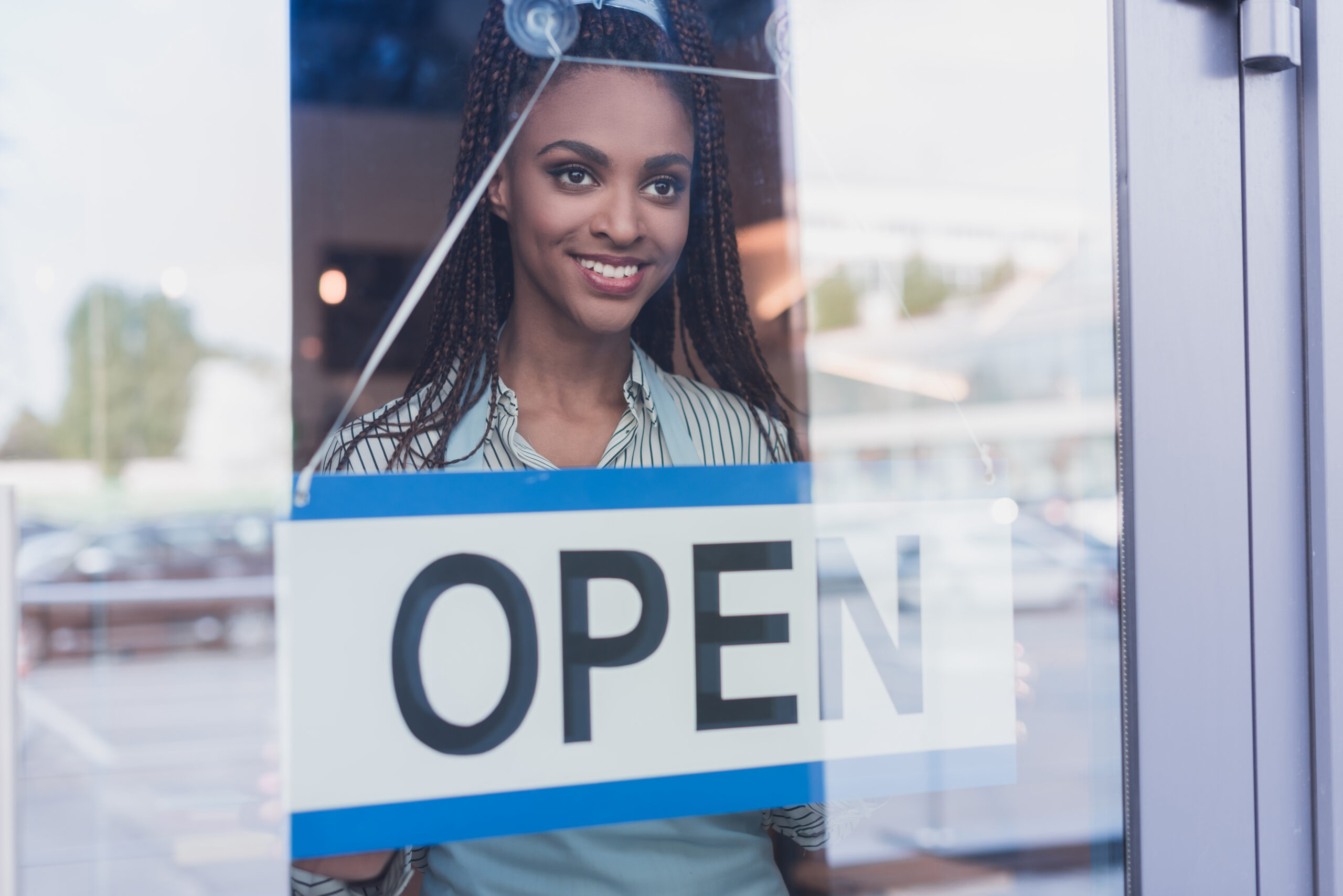 Open sign displayed on a glass storefront door with a smiling employee inside.