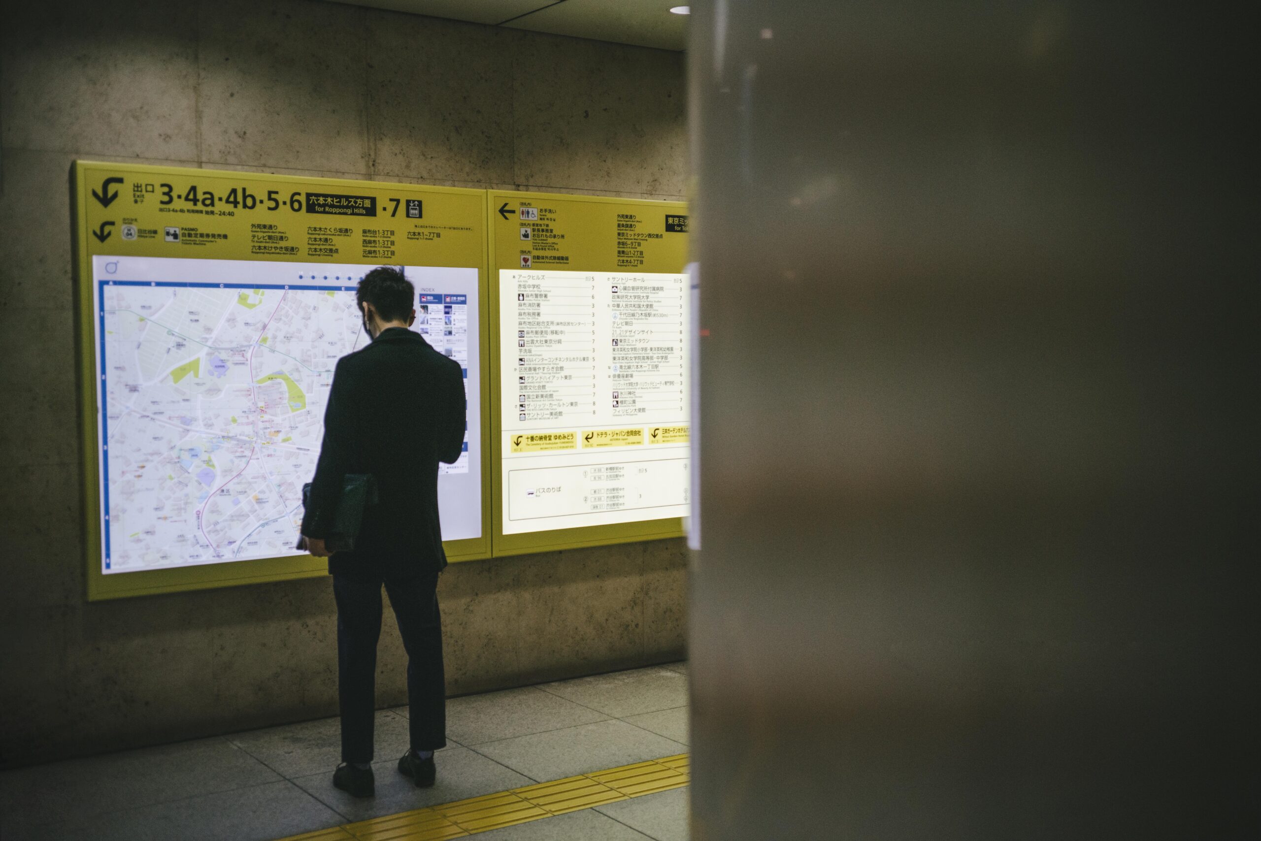 Man reading an outdoor bulletin board with posted notices and information displayed in a public station area